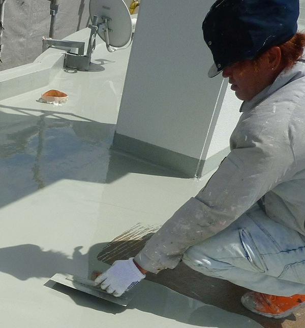 屋上への防水塗装の作業風景。塗料の機能を最大限に引き出せるよう、職人が丁寧に仕上げていく